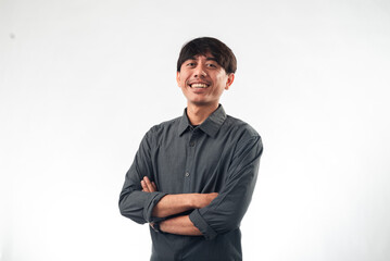 A smiling Asian man in a dark grey button-up shirt stands confidently with arms crossed against a plain white background, ideal for professional headshots, corporate profiles, or personal branding