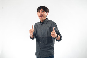 Fototapeta premium A cheerful Asian man in a dark grey button-up shirt gives double thumbs-up gestures against a plain white background, ideal for positive messaging, personal branding, or business profile content