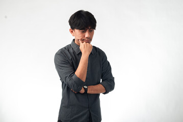 An Asian man in a gray shirt with a thoughtful expression, hand on chin, and one arm crossed,...