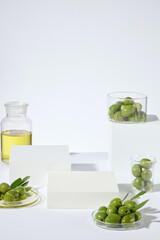 High angle shot photo on white background with some empty podiums for natural cosmetic displaying, dotted with green color of fresh olives and yellow olive oil. Copy space for text