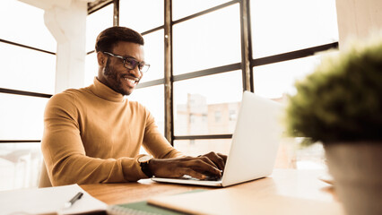 Office Work Concept. Smiling black businessman working on laptop in modern office. Panorama, free space