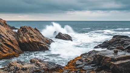 Fototapeta premium A dramatic coastal scene with waves crashing against rocky formations under a cloudy sky.