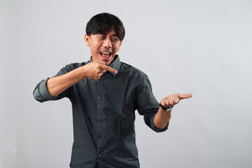 Smiling Asian man in a gray shirt pointing at his open palm, presenting something imaginary, against a plain white background. Perfect for showcasing products, services, or promotional content.