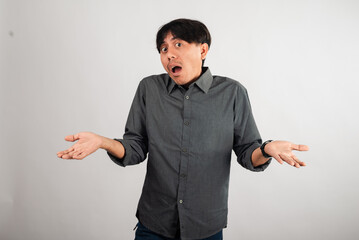An Asian man in a gray shirt shrugging with both hands up, expressing uncertainty or confusion. He...