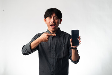 An Asian man in a gray shirt smiling broadly while pointing to a smartphone he holds in his other...
