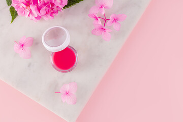 A round cosmetic jar with a delicate pink lip balm on a marble podium. The concept of moisturizing, nutrition, natural cosmetics for lip skin care.