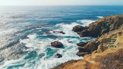 Fototapeta premium A scenic coastal view showcasing waves crashing against rocky cliffs under a clear sky.