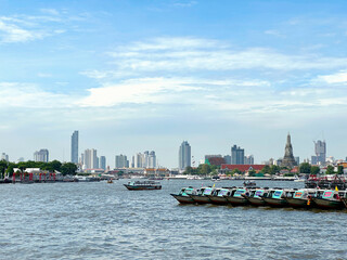 Naklejka premium View of the Chao Phraya River and the service boats parked at Wat Arun Ratchawararam and the city behind.