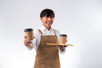 Asian barista in a white shirt and brown apron smiling while holding a tray with two disposable...