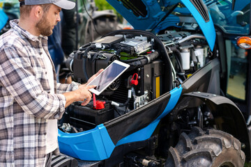 Man agricultural machinery mechanic diagnoses tractor engine operation using digital tablet. © Barillo_Images