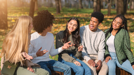 Black guy telling his international teen friends funny stories while spending weekend at park