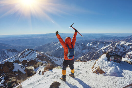 Climber or alpinist at the top of a mountain. A success of mountaineer reaching the summit. Outdoor adventure sports in winter alpine moutain landscape.