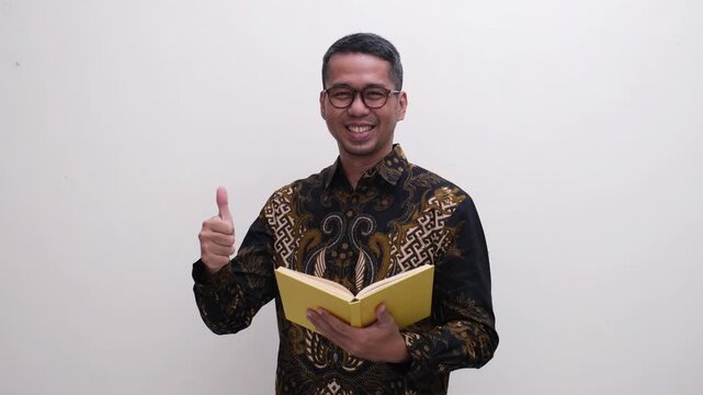 A man smiling and give thumbs up at the camera while holding a book
