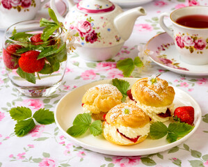 Cream puffs cakes or profiterole filled with whipped cream and served with strawberries and tea on the table
