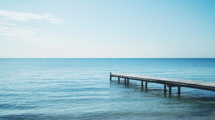 Fototapeta premium A serene view of a wooden pier extending into calm blue waters under a clear sky.