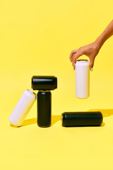 Minimalistic mockup with black and white cans on yellow background, with hand picking up one can....