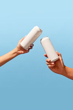 Sparking tea. People holding two white cans against light blue background. Mockup. Beer, lemonade, energy drinks, soda water. Ideal for branding and product placement with focus on modern aesthetics.