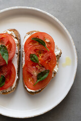 Breakfast toasts with cream cheese, fresh tomato, olive oil and baby spinach on a white plate. Healthy tasty food concept, top view