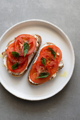 Breakfast toasts with cream cheese, fresh tomato, olive oil and baby spinach on a white plate. Healthy tasty food concept, top view