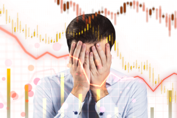 A man holds his face in frustration in front of a stock market graph showing declining trends on a white background, signifying financial distress