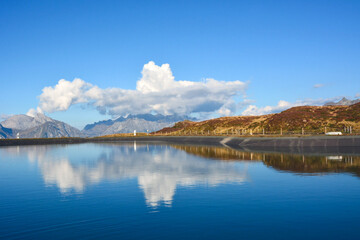 A view of a large lake in front of the mountains in which the blue sky with clouds is reflected. Natural tourist landscape