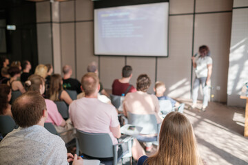 Group of people engaged in business seminar with speaker presenting. Professional presentation setting with attentive audience and informative slide on screen.