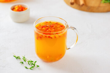 Cup of sea buckthorn tea with orange, cinnamon and thyme on white table. Healthy herbal autumn drink.