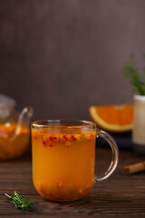 Sea buckthorn tea with orange, cinnamon and thyme in glass on a brown wooden table. Herbal vitamin tea. Hot autumn drink. Vertical orientation.