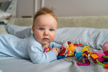 A baby explores a variety of toys while lying on a bed, showing curiosity and engagement in a cozy environment