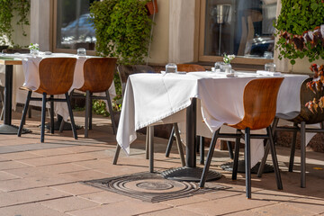 Empty outdoor tables with white tablecloths await diners in a vibrant urban setting