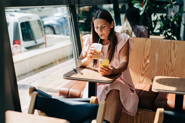 A middle-aged woman sits at a table in a cafe in the summer and uses a mobile phone to communicate.