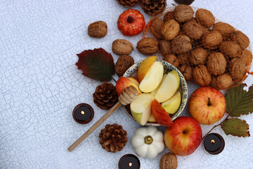 Autumn still life with apples, nuts, red leaves and candles on a table. Textured background with space for text. 