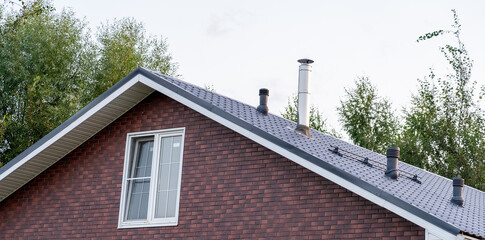 A brick house features a sloped roof and visible chimney under a clear sky with trees in the background