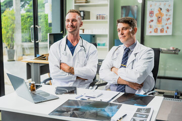 Fototapeta premium Caucasian middle-aged male doctor and Italian scientific researcher are seated at desk, discussing innovative antiviral drug inventions, with a monitor displaying the latest technology advancements.