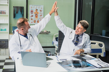 Obraz premium Caucasian middle-aged male doctor and Italian scientific researcher are seated at desk, discussing innovative antiviral drug inventions, with a monitor displaying the latest technology advancements.