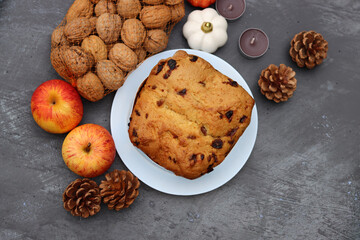 Raisin fruit cake dessert traditional pastry dried fruits, nuts, apples, cones and candles on dark grey background with copy space. Autumn menu ideas. 