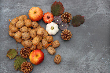 Autumn background. Apples, nuts, fir cones, candles and autumn leaves on dark textured table with space for text.  