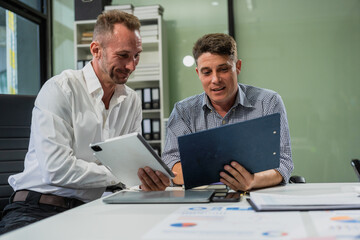 Caucasian middle-aged male businessperson and an Italian accountant are seated at a desk, engaging in a professional meeting, discussing various aspects of technology and innovation in their fields.