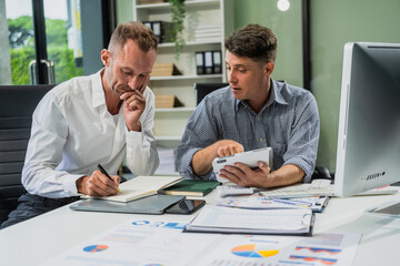 Caucasian middle-aged male businessperson and an Italian accountant are seated at a desk, engaging in a professional meeting, discussing various aspects of technology and innovation in their fields.