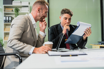 Caucasian middle-aged male businessperson and an Italian accountant are seated at a desk, engaging in a professional meeting, discussing various aspects of technology and innovation in their fields.