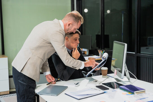 Caucasian middle-aged male businessperson and an Italian accountant are seated at a desk, engaging in a professional meeting, discussing various aspects of technology and innovation in their fields.