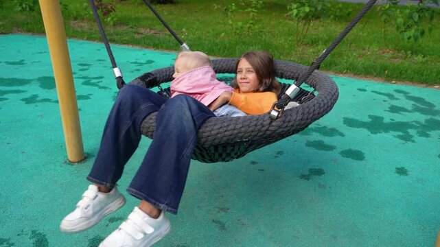 Two kids are happily swinging together at a park, sharing laughter and joy in the warm afternoon sun