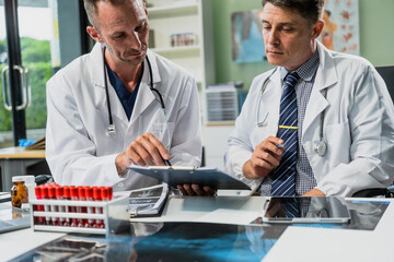Caucasian middle-aged male doctor and Italian scientific researcher are seated at desk, discussing innovative antiviral drug inventions, with a monitor displaying the latest technology advancements.