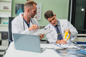 Caucasian middle-aged male doctor and Italian scientific researcher are seated at desk, discussing innovative antiviral drug inventions, with a monitor displaying the latest technology advancements.