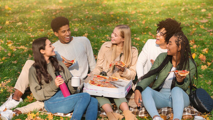 Carefree multiethnic hipsters enjoying take away pizza, having picnic in forest