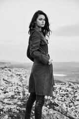 Majestic woman in trench coat standing on mountain summit overlooking ocean view