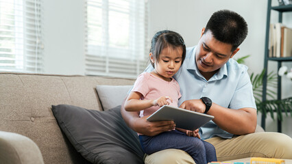 Young girl and single father are sitting using digital tablet to teach daughter learning. Researching for work, tests or exams. Technology, Education.