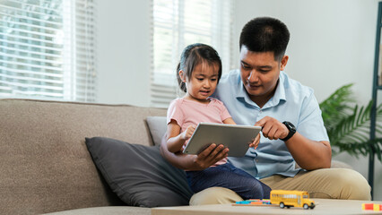 Young girl and single father are sitting using digital tablet to teach daughter learning. Researching for work, tests or exams. Technology, Education.