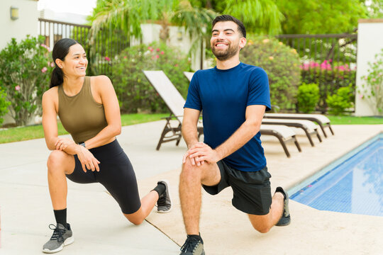 Man and woman in athletic clothing smiling as they stretch by the pool following an outdoor workout