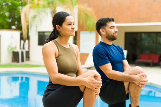 Young hispanic couple wearing sportswear doing stretching exercises by the poolside